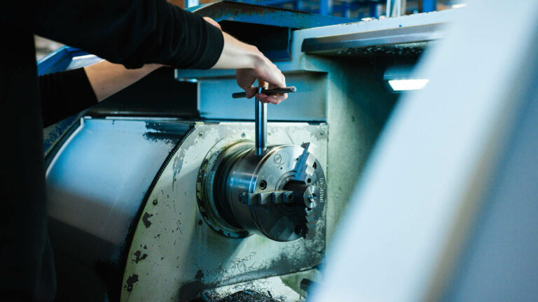 Nahaufnahme der Hand eines Maschinenbediener, der mit einem T-Schlüssel ein Dreibackenfutter an einer Metalldrehmaschine einstellt.