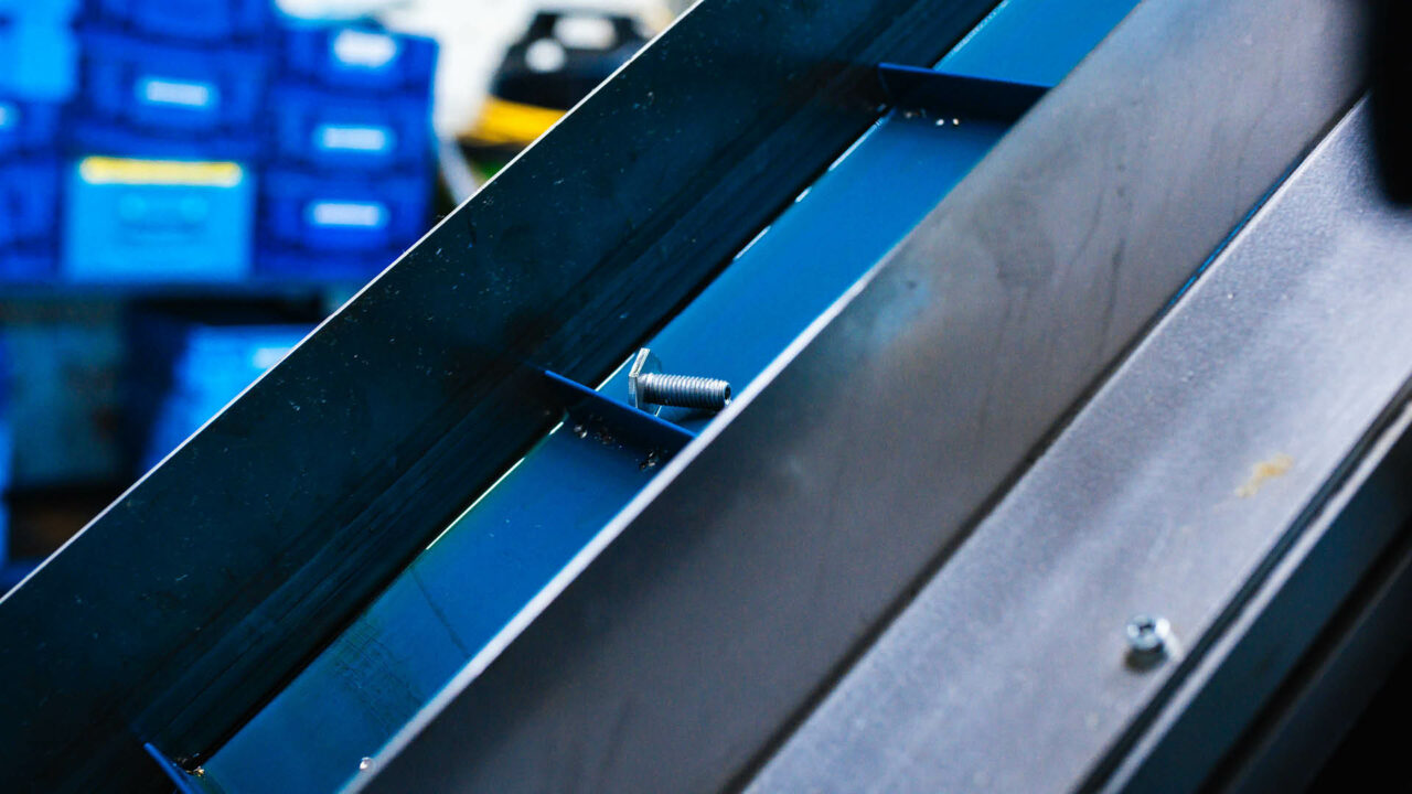 Eine einzelne, silberne Metallschraube liegt in einer blauen Führungsschiene im Detail.