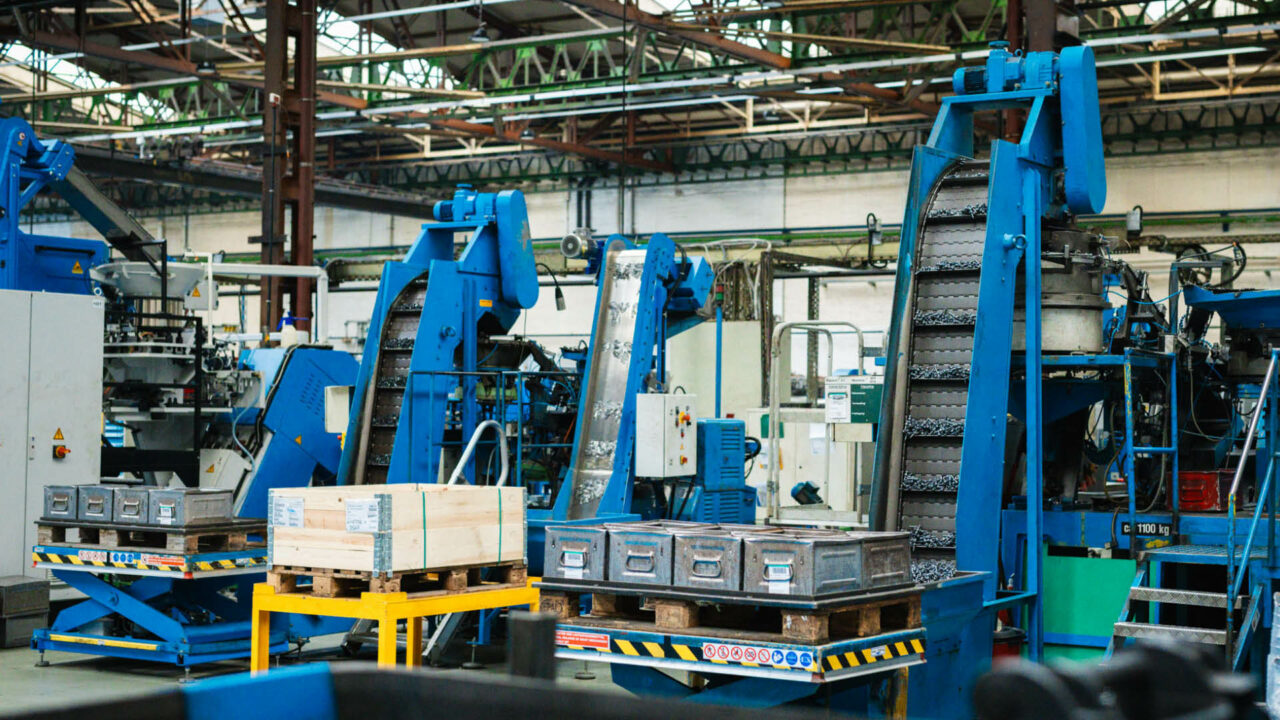 Blick in eine Industriehalle mit zwei großen, blauen Förderbändern, die Schrauben transportieren.